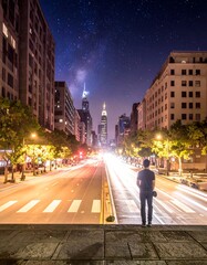 Fototapeta premium A lone figure gazing at bright city lights and starry night sky