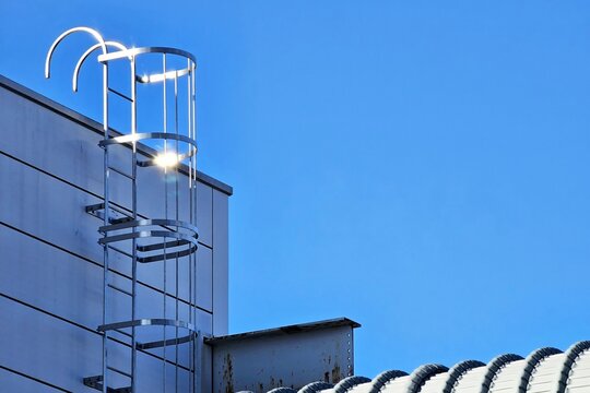 Minimal fixed aluminum ladder with a safety cage with blue sky background.