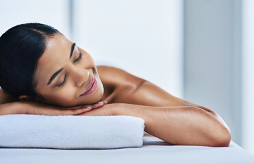 Fototapeta premium Relax, girl and smile on massage table at spa for luxury pamper, muscle therapy or space. Hospitality, woman and peaceful at wellness resort for holistic treatment, body care or zen for stress relief