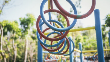 Colorful monkey bar rings on a playground climbing structure in a park, shallow depth of field, sunny day and blurred trees in background. © Phushutter