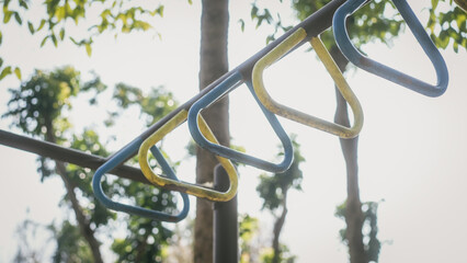 Close-up of outdoor playground monkey bars with blue and yellow handles, shallow depth of field and sunlit trees in the background. © Phushutter
