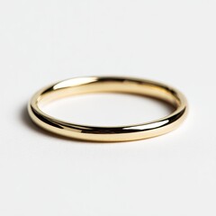 Gleaming, simple gold band ring displayed on a bright white surface, casting a subtle shadow