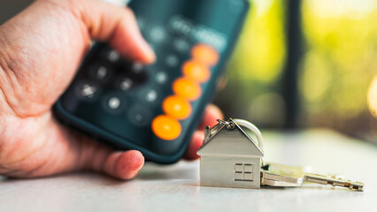 Person using calculator on smartphone with house key for real estate financial planning, mortgage...