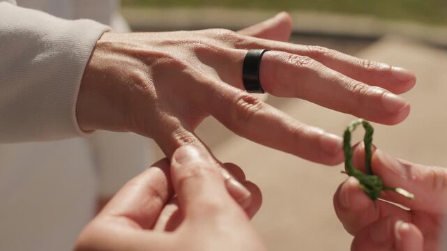 Tender hands offer wedding ring symbolizing love. Sunlit outdoor scene capturing intimate wedding ring placement. Heartfelt moment in park where two hands exchange wedding bands affectionately