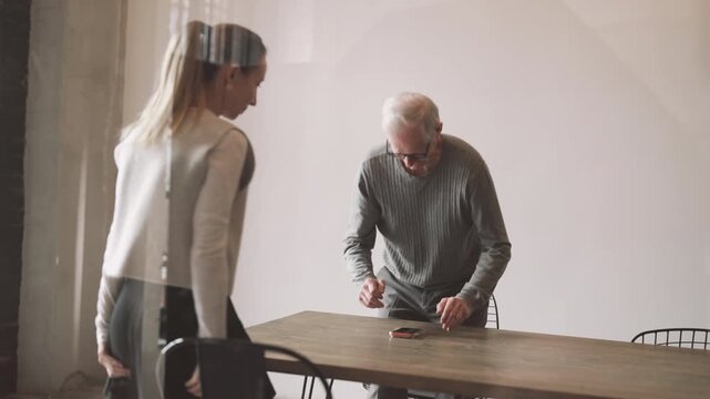 Old man greeting young adult woman in office, job interview in marketing company . Female candidate and male boss shaking hands and sitting down at table in conference hall in modern office, business