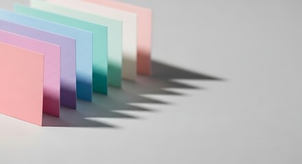 Fototapeta premium Colorful paper sheets arranged in a row, casting shadows on a gray surface.