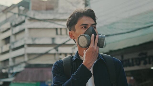 A young man wears a face mask to protect himself from PM 2.5 smoke, urban particulate matter, air pollution from vehicle exhaust, and toxic smog from industrial factories.