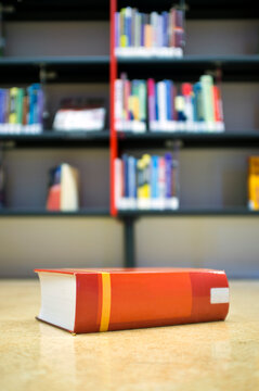 A library book on the floor in front of a bookshelf in a public library, space on the shelves.