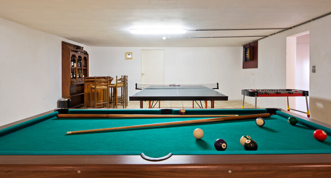 Interior view of a basement room with pool billiard and ping pong tables.