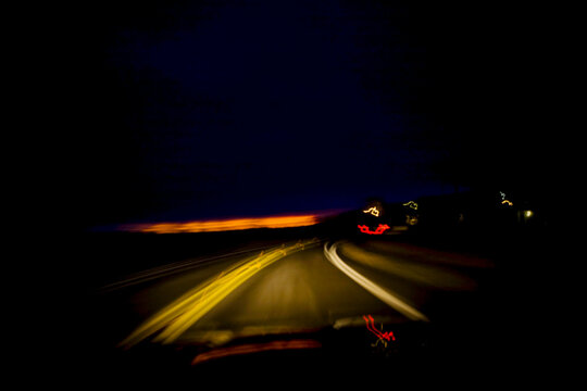 Blurred driver's view of a roadway at night through the windshield.