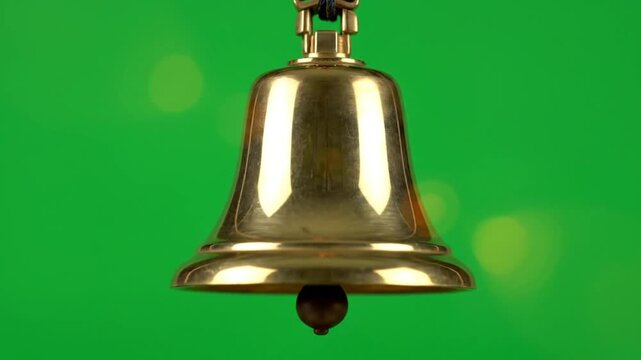 Close-up shot of a golden bell with a wooden clapper ringing, against a blurred green background
