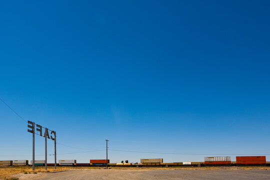 Cafe Sign, a tall sign by the railroad track, a freight train and box cars on the rails.