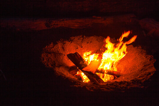 Beach fire along Puget Sound at night, glowing embers and flames rising, camp fire