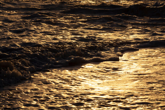 Ocean waves breaking on the shore at sunset, light reflecting off the water.
