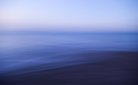 View across a seascape to the horizon, flat calm water surface and blurred motion.