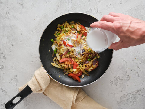 Cooking a vegetable stir-fry with rice in a pan while adding milk in a kitchen setting