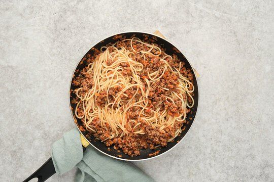Cooked pasta with meat sauce in a large frying pan on a light surface during a meal preparation
