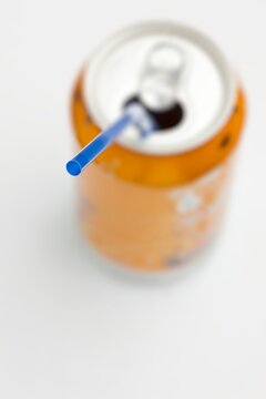 Blue straw inserted into open orange soda can with white background. Creative minimal concept for refreshment or beverage themes.