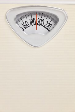 Analog bathroom scale close-up with red needle pointing near 200 pounds. Health and weight loss concept on neutral background.