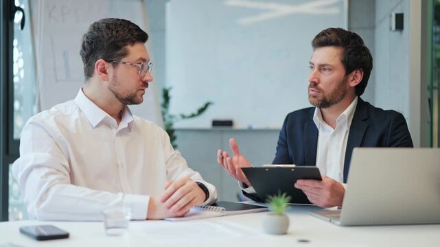 Focused business professionals in an important office meeting. They calmly collaborate on strategies reviewing documents discussing new ideas with confident expressions, conveying dedication, teamwork