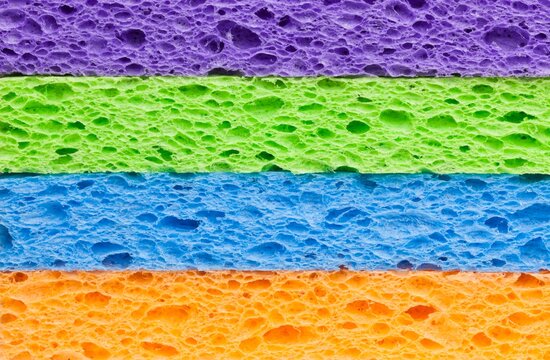 Macro image of a neatly stacked set of brightly colored synthetic cleaning sponges in vibrant purple, green, blue, and orange. 