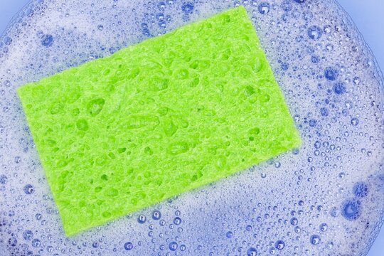Close-up of a vibrant green sponge resting in a bowl of foamy soapy water., bubbles and foam. 