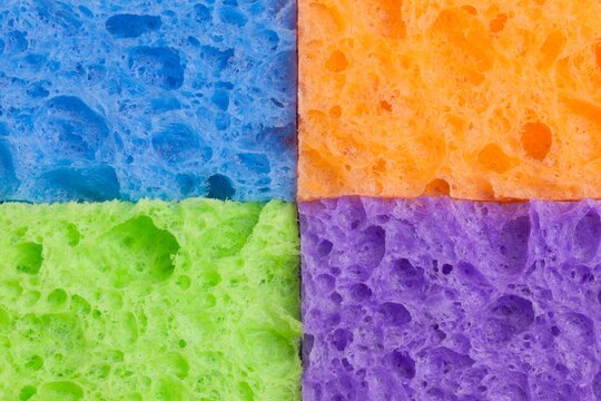 Close-up of four household sponges arranged in a square grid pattern with vivid colors - blue, orange, green, and purple, cleaning, home care, or color design concepts.