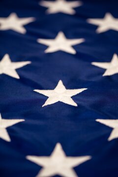 Macro detail of multiple white embroidered stars on the blue field of the American flag