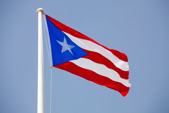 The Puerto Rican flag flutters boldly in the wind against a clear blue sky. 