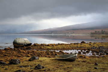 Lonely rowing boat on rocky shore of a misty loch © Janica