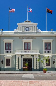 Front view of the Casa Alcaldia, the historic city hall building in Ponce, Puerto Rico, with flags flying under a clear blue sky and classic neoclassical architecture.