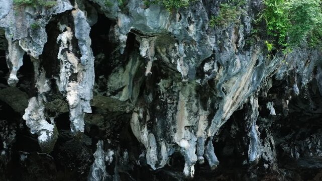 Stunning rock formations in Viking Cave, Thailand, showcasing intricate stalactites and lush greenery along the rugged cliffside above the tranquil turquoise waters below