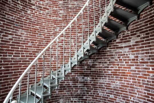 A view of the metal spiral staircase winding up inside the Umpqua Lighthouse in Winchester Bay, Oregon, an exposed red brick wall and winding stairs.