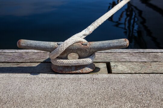 Close-up of a dock cleat with rope securely tied, taken at Charleston Marina in Oregon. The weathered textures of the metal and wood add a maritime feel to this nautical detail scene.