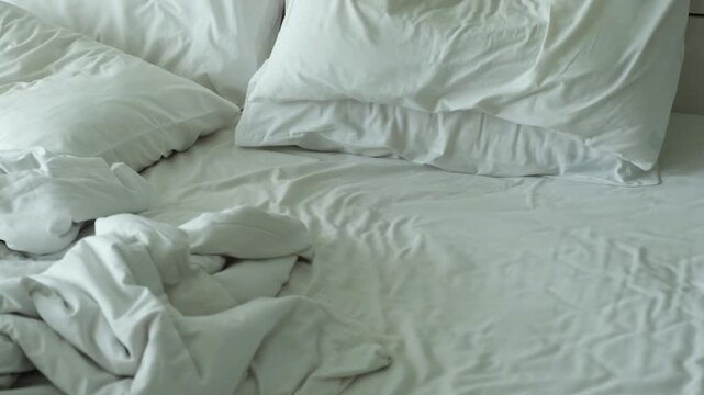 Unmade bed with wrinkled white linens and pillows in disarray, showcasing a cozy yet untidy bedroom setting from a top view perspective