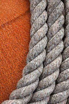 Close-up of weathered nautical rope coiled against the textured surface of a rusted buoy in Bandon, Oregon.