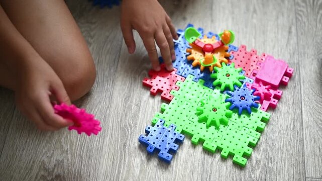 Bright plastic gear set arranged on floor while boy builds mechanism by hand. Gear toy demonstrates logical thinking, creativity, and engaging educational childhood activity at home.
