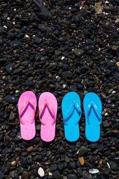 A pair of pink flip flops and a pair of blue flip flops lie side-by-side on a rocky beach in Florence, Oregon.