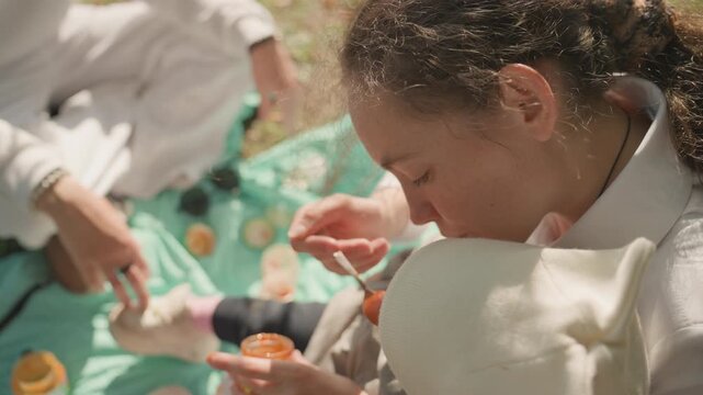 Daughter tasting jam during family picnic, mint blanket spread on grass, parent hands offering spoon and jar, warm golden sunlight, candid closeup of feeding and sharing, gentle nurturing, slow