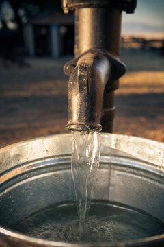 Close-up of water flowing from an old metal pump into a galvanized steel bucket. Rural utility scene captured at sunset on Antelope Island, Utah.