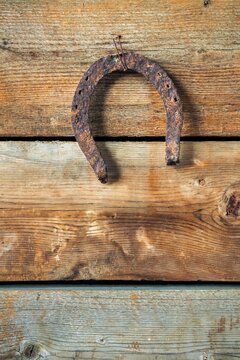 A weathered, rusted horseshoe hangs upside down on an aged wooden plank wall, symbolizing tradition and good luck.