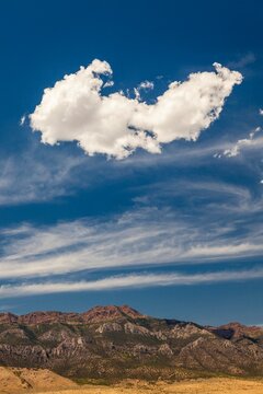 A large cloud drifts over rugged Utah mountains, framed by streaks of high-altitude cirrus clouds and deep blue sky.