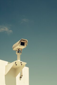 Close-up of a surveillance camera mounted outdoors against a clear blue sky, symbolizing security and monitoring.