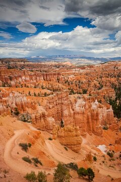Striking view of Bryce Canyon's hoodoo formations and orange cliffs under a dramatic sky. A rugged trail winds through the vibrant Utah landscape.