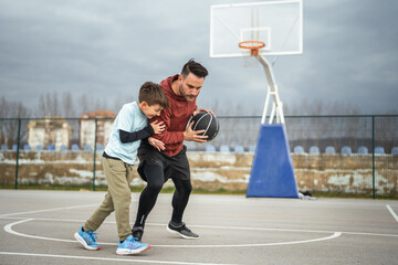 Father and son playing basketball on outdoor court