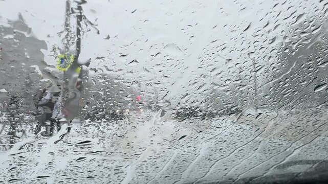 View from car windshield in snowy weather, wipers not working, raindrops and snow blurring the road ahead and reducing visibility.