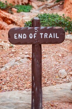 A rustic wooden 'End of Trail' sign marks the conclusion of a hiking path in Bryce Canyon National Park, set against reddish gravel and weathered desert wood.