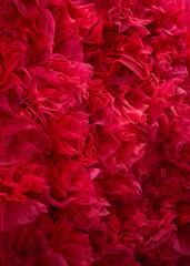 Fototapeta premium Vibrant red tulle fabric texture. A dense arrangement of ruffled and layered soft mesh material, creating a voluminous and romantic abstract background for fashion or floral concepts.