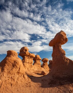 Cluster of unique hoodoo rock formations in Goblin Valley State Park, Utah, rising from the desert floor beneath a vivid blue sky with scattered clouds.