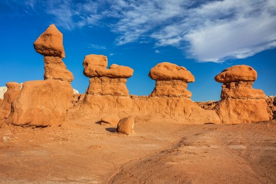 Eroded sandstone hoodoo rock formations under a bright blue sky with scattered clouds in Goblin Valley State Park, unique sandstone structures in warm red rocks.